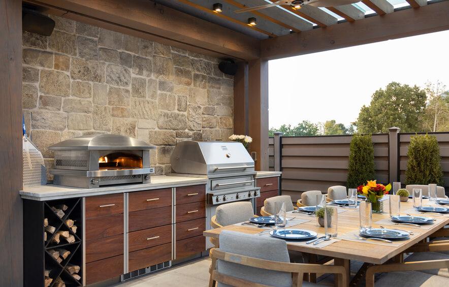 Outdoor kitchen with stone wall, grill, and dining table set.