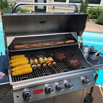 Stainless steel grill with food on a patio by a pool