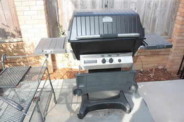 Black barbecue grill on a patio with chairs and a fence in the background